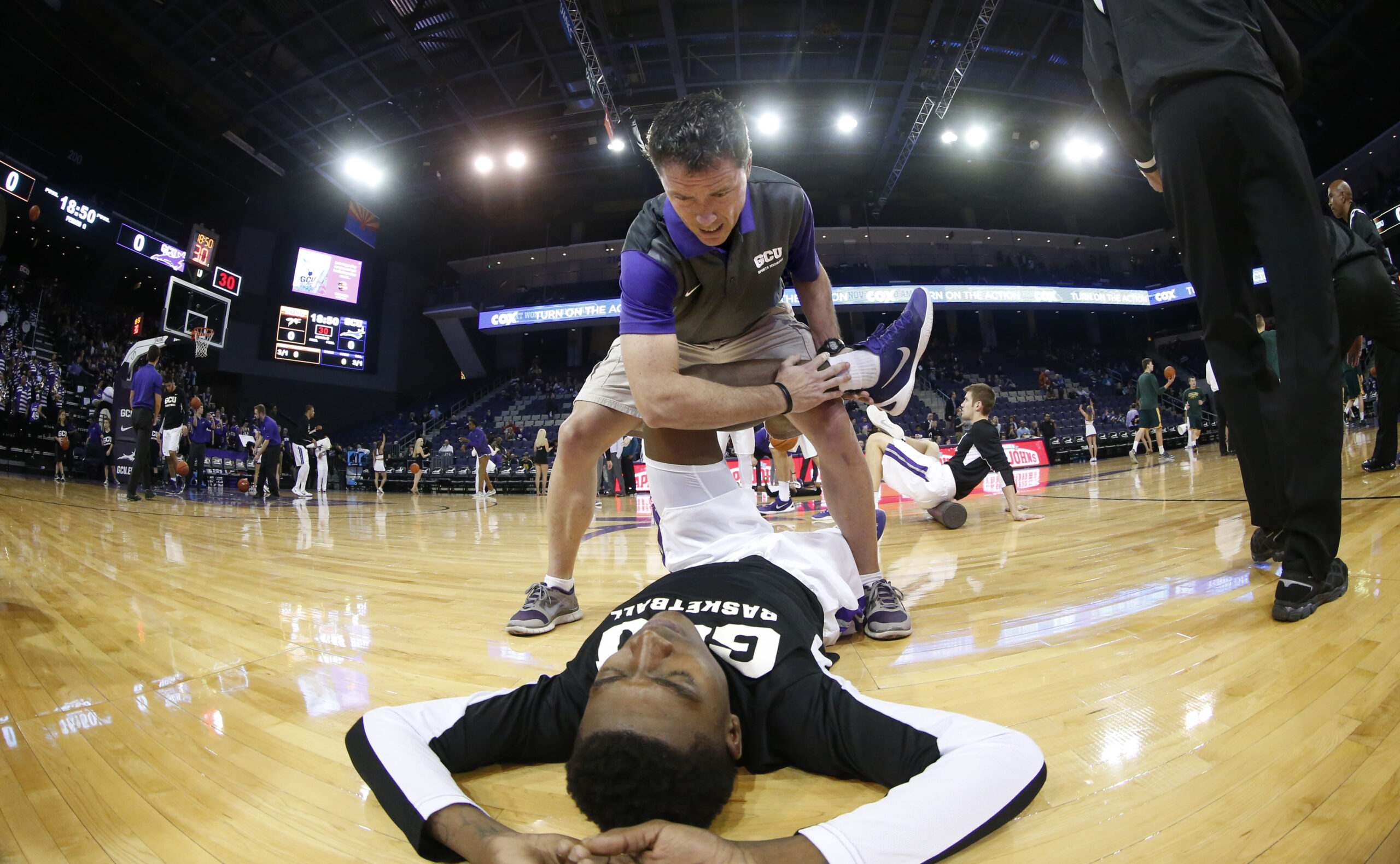 GCU's Geordie Hackett, MS, ATC, CSCS works with an athlete on the floor during pregame warm ups. He also works with the IRON COURTS staff.